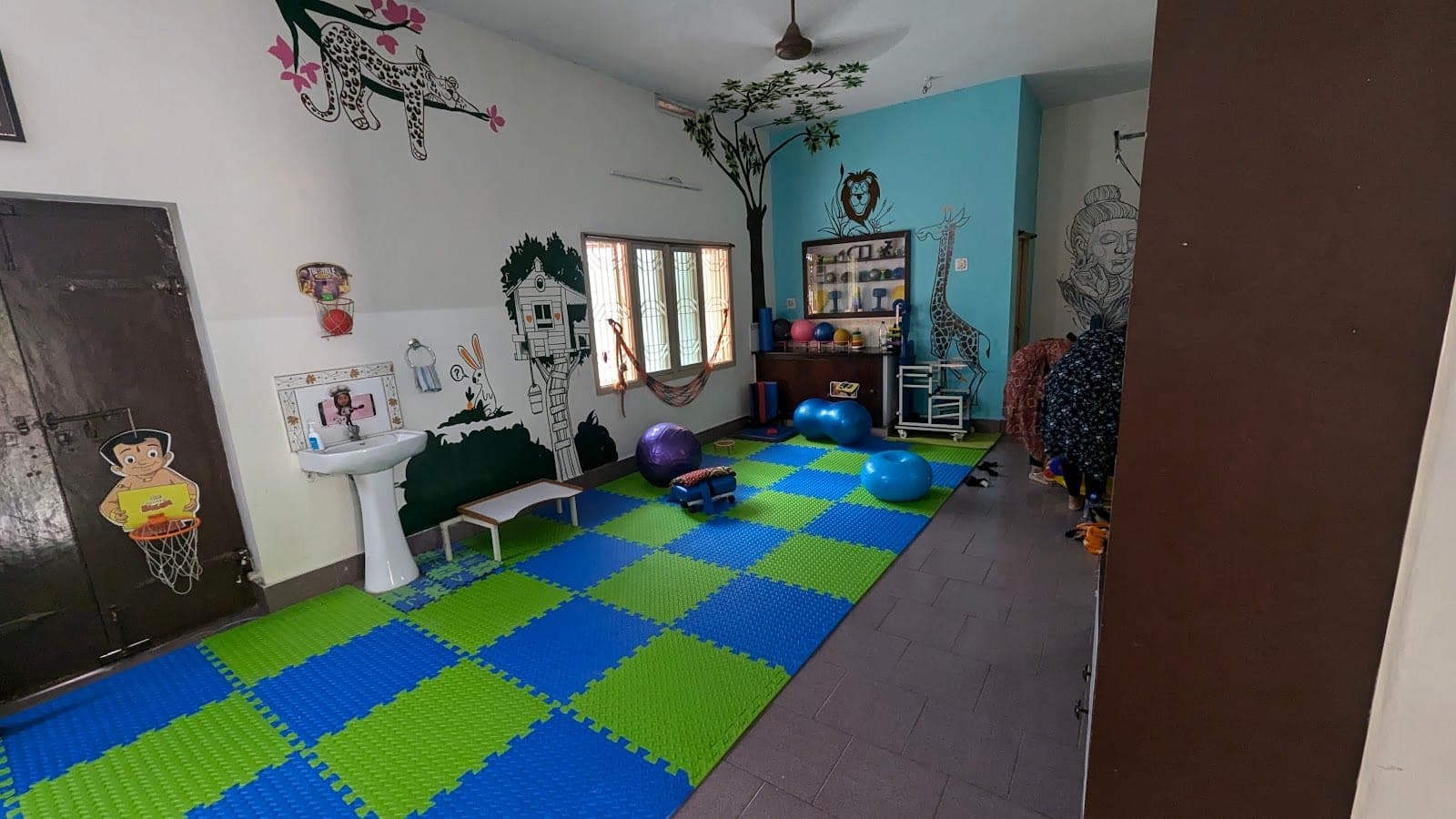 Pediatric physiotherapy hall at Thera360 with a colourful interlocking floor mat, animal wall murals, gym balls and exercise equipment